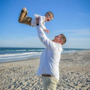 Groom and baby son laughing on beach packages fees